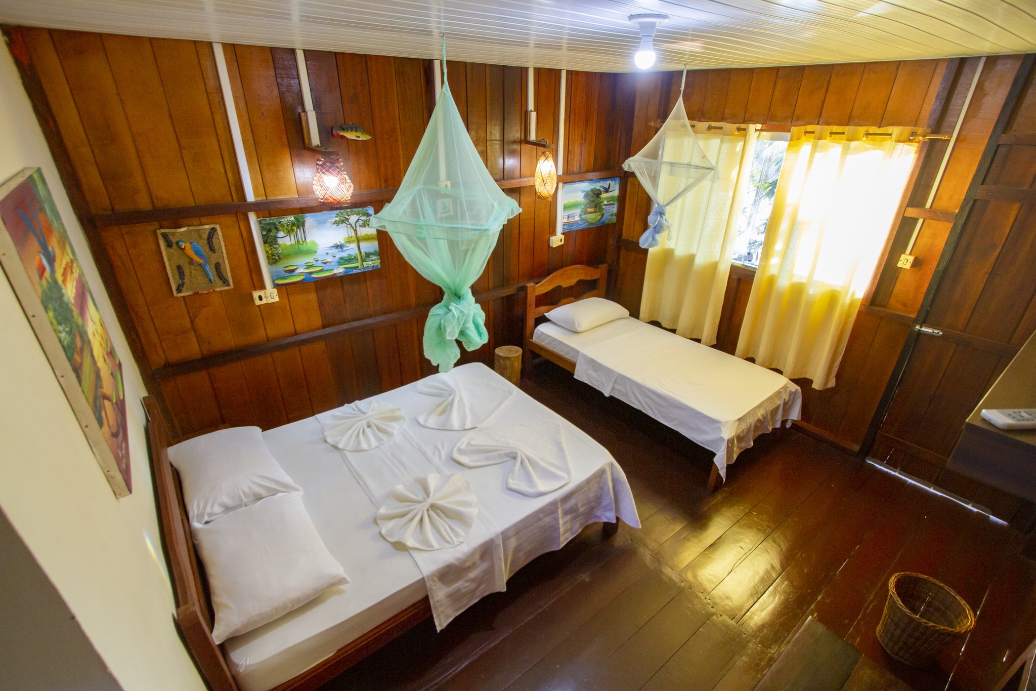 Towel art and tidy nets greet you in the warm wooden bungalow interior. Photo: David Nascimento @ Interior of a wooden bungalow with double and single beds, mosquito nets and decorative towel art