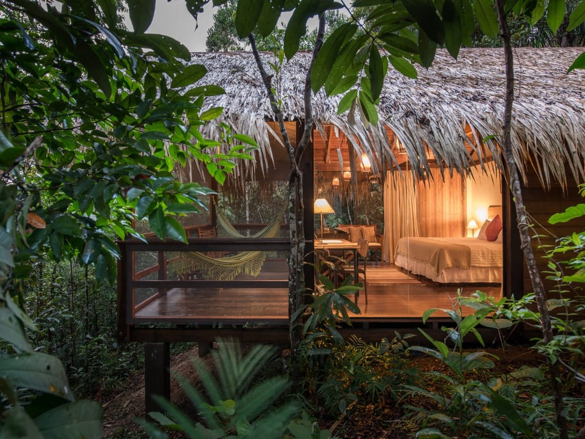 Amazon jungle lodge bungalow on stilts with a hammock and lit bedroom surrounded by rainforest