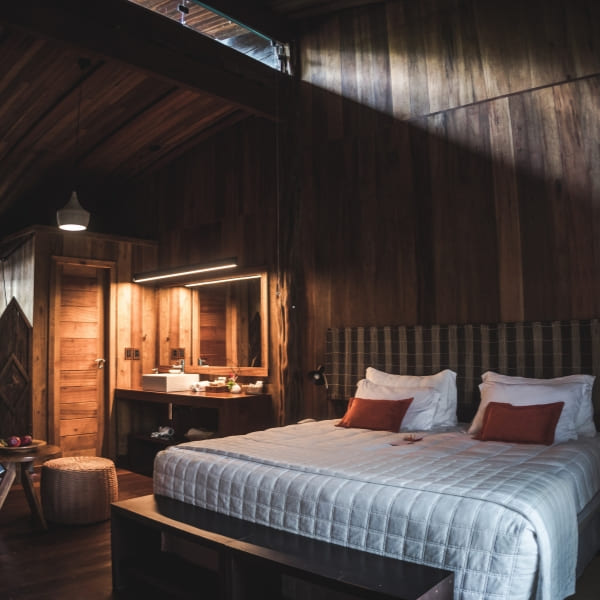 A wood-panelled suite bedroom with a large bed, orange cushions and a mirror-lit vanity at a luxury Pantanal lodge.