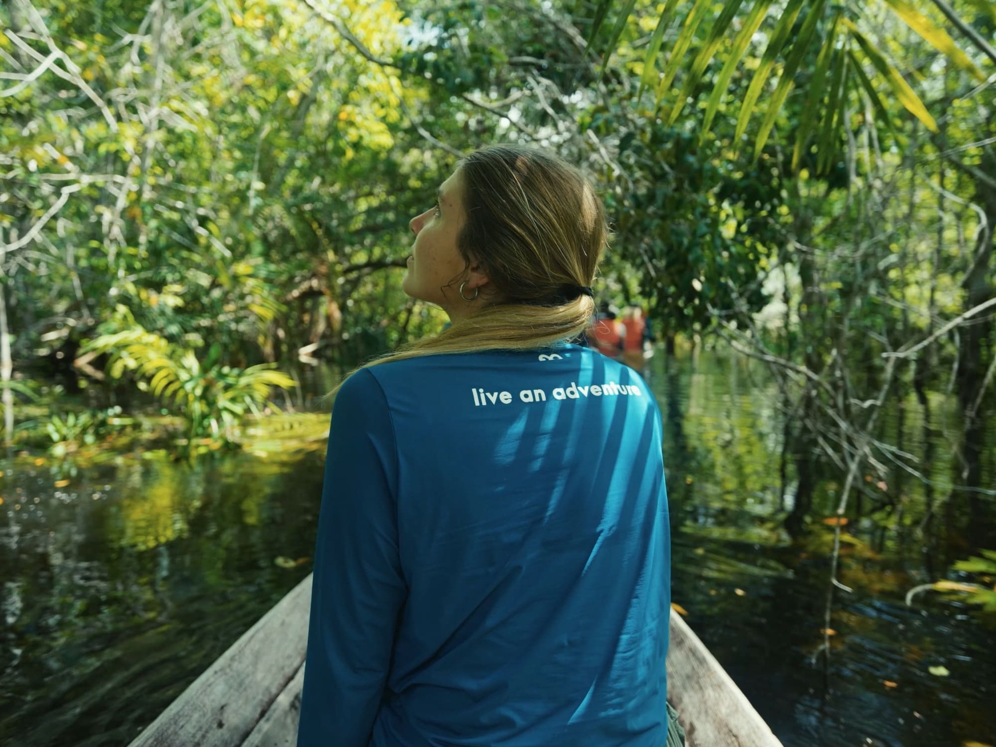 Traveler in a wooden canoe gazing up at the flooded rainforest canopy on an Amazon adventure