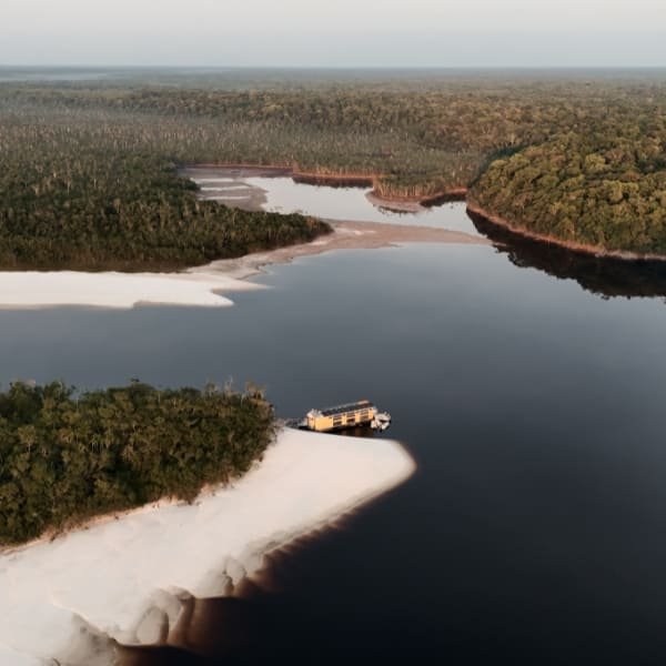 Aerial view of an Amazon river cruise boat moored at a white-sand river beach at sunset
