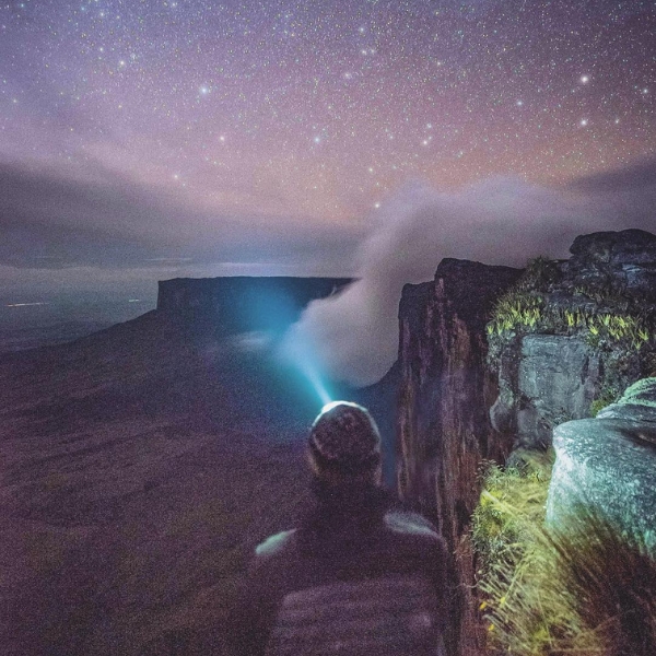 A starry night sky over Mount Roraima with a trekker's headlamp glowing