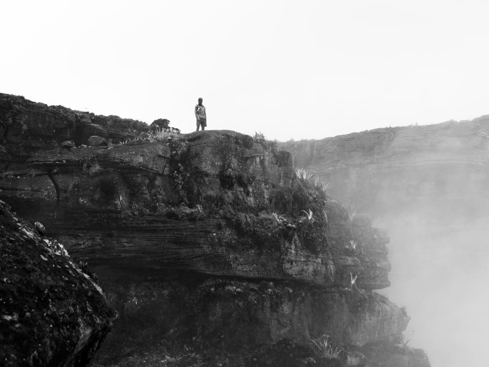 A hiker on a misty cliff at the summit of Mount Roraima, in black and white