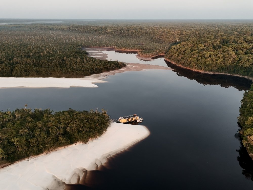 Vista aérea de un crucero de lujo por el Amazonas amarrado junto a una playa de arena blanca rodeada de selva, en Brasil.