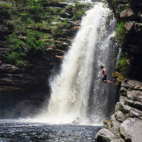 Ein Schwimmer springt in den Naturpool unter einem Wasserfall in der Chapada Diamantina, Brasilien.