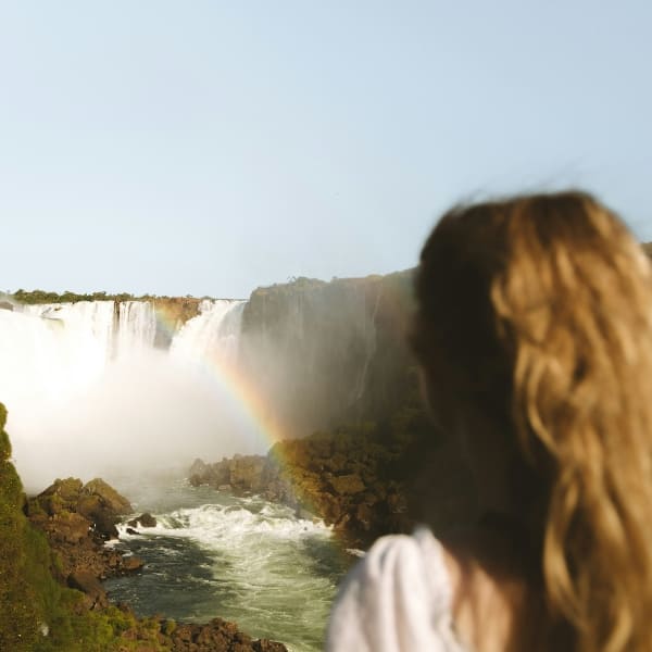 Eine Besucherin blickt über die Iguaçu-Wasserfälle, mit einem Regenbogen in der Gischt, Brasilien.