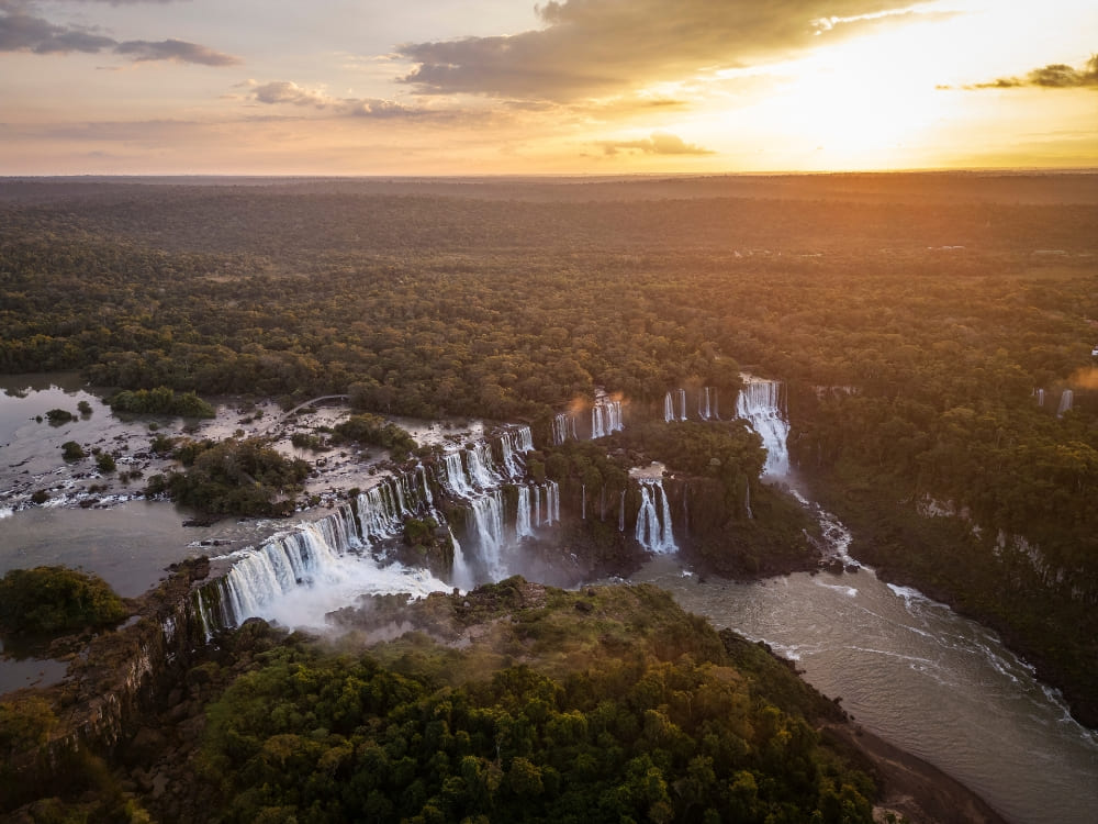 Luftaufnahme der Iguaçu-Wasserfälle bei Sonnenuntergang, umgeben vom Atlantischen Regenwald in Brasilien.