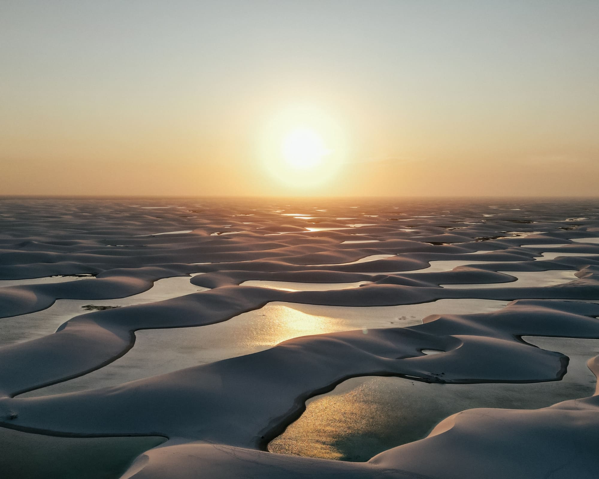 Luftaufnahme der weißen Sanddünen und Regenwasserlagunen der Lençóis Maranhenses bei Sonnenuntergang, Brasilien.