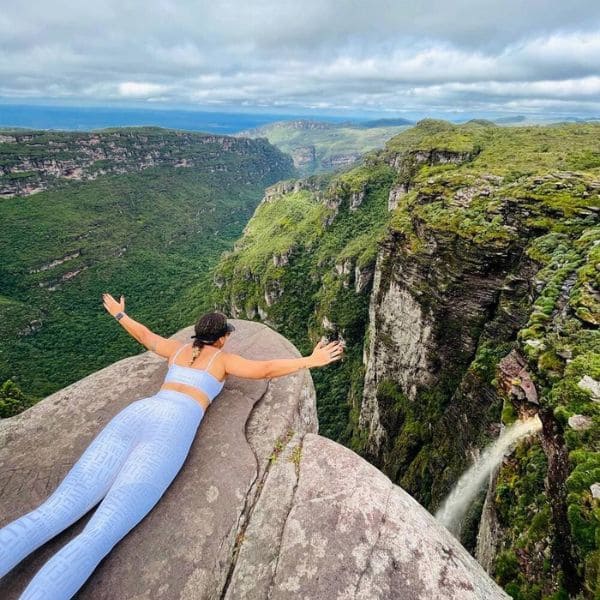 Eine Wanderin liegt mit ausgebreiteten Armen am Rand des Aussichtspunkts Cachoeirão über dem Canyon des Vale do Pati, Chapada Diamantina, Brasilien.