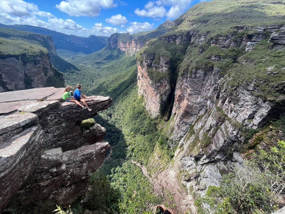 Zwei Wanderer sitzen auf einem vorspringenden Felsen über dem Canyon des Vale do Pati in der Chapada Diamantina, Brasilien.