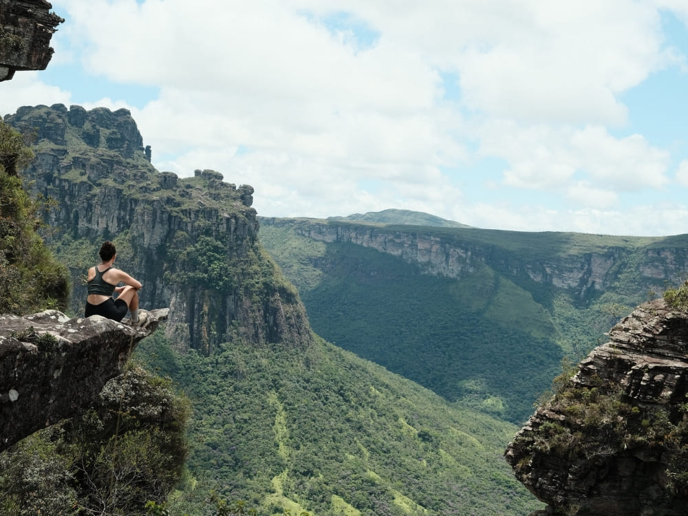 Eine Wanderin sitzt auf einem Felsvorsprung über einem grünen Tal in der Chapada Diamantina, Bahia, Brasilien.