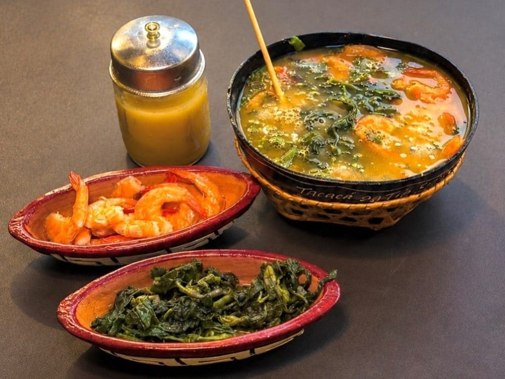 Eine Cuia Tacacá mit Jambu und getrockneten Garnelen, daneben Schälchen mit Garnelen, Jambu und ein Glas Tucupi