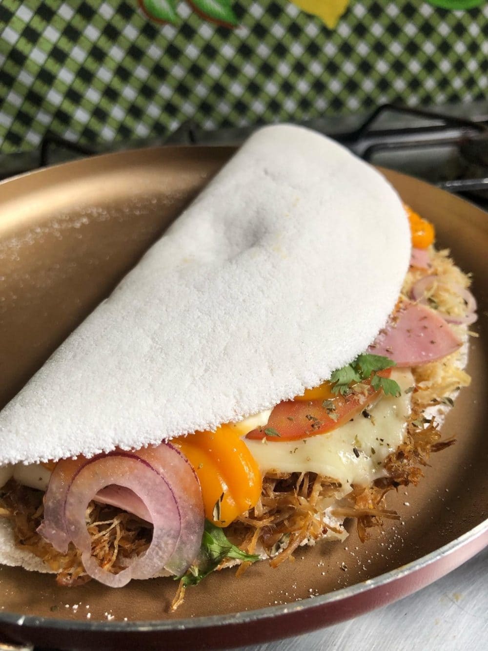 Zusammengeklappte Tapioka-Crêpe mit geschmolzenem Käse, Zupffleisch, Tomate, Zwiebel und Pimenta-de-cheiro