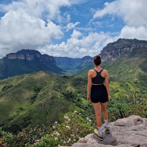 Eine Wanderin auf einem Felsen blickt über das grüne Tal und die Tafelberge des Vale do Pati, Chapada Diamantina, Brasilien.