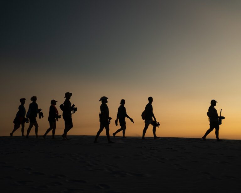 Silhouettes of a small trekking group walking across the Lençóis Maranhenses dunes at sunset
