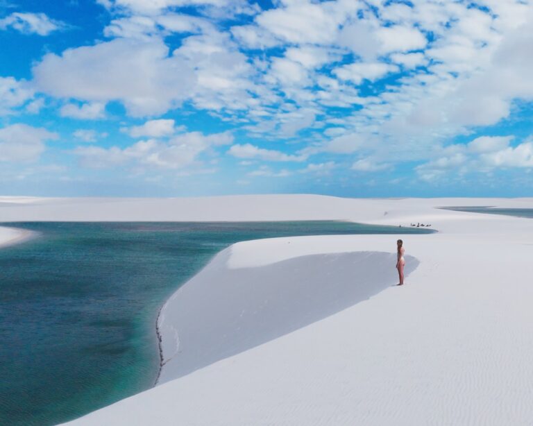 Woman standing on a white dune above a turquoise lagoon in Lençóis Maranhenses under a blue sky