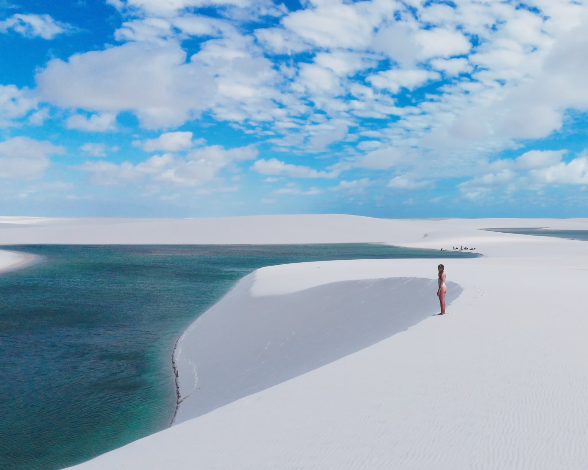 Femme debout sur une dune blanche au-dessus d’une lagune turquoise dans les Lençóis Maranhenses, sous un ciel bleu