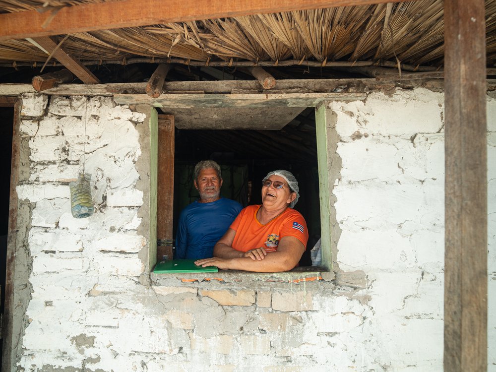 Dona Dete et Seu Moacir souriant à la fenêtre de leur maison dans l’oasis de Baixa Grande