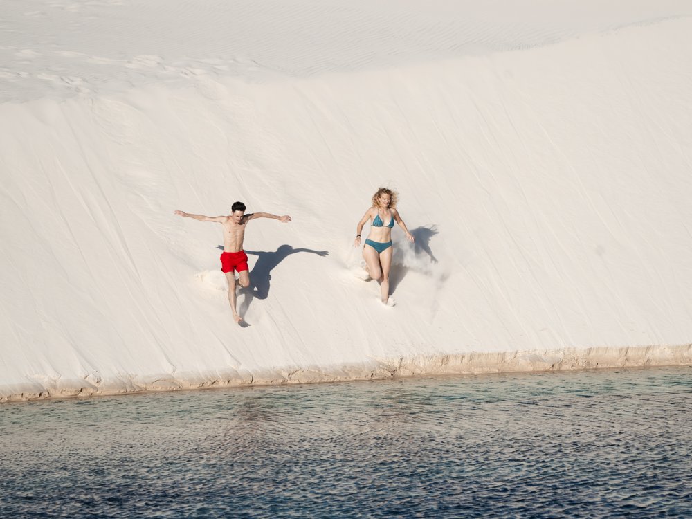 Deux voyageurs dévalant une dune blanche vers une lagune dans les Lençóis Maranhenses