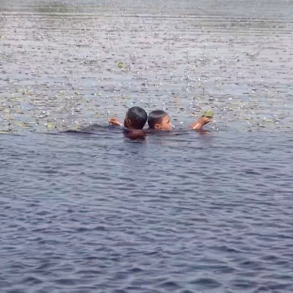 Dos niños nadan en una laguna de los Lençóis Maranhenses, uno de ellos sostiene una hoja sobre el agua