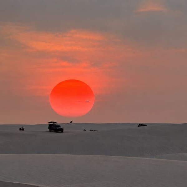 Véhicules 4x4 sur les dunes sous un grand soleil rouge couchant aux Lençóis Maranhenses