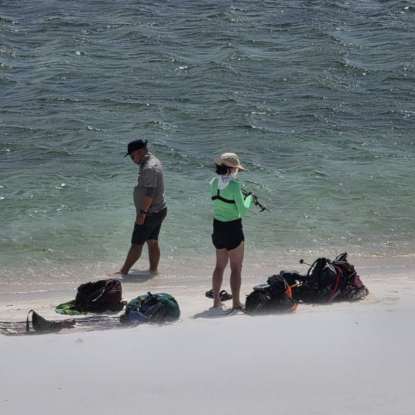 Jihee Yeon and a crew member on a lagoon shore, with their filming gear on the sand