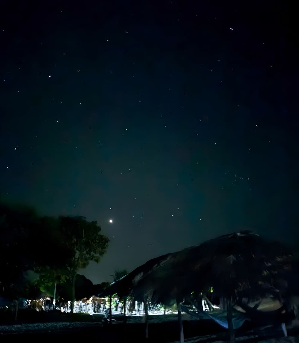 Starry night sky over thatched shelters and hammocks on the Lençóis Maranhenses trek