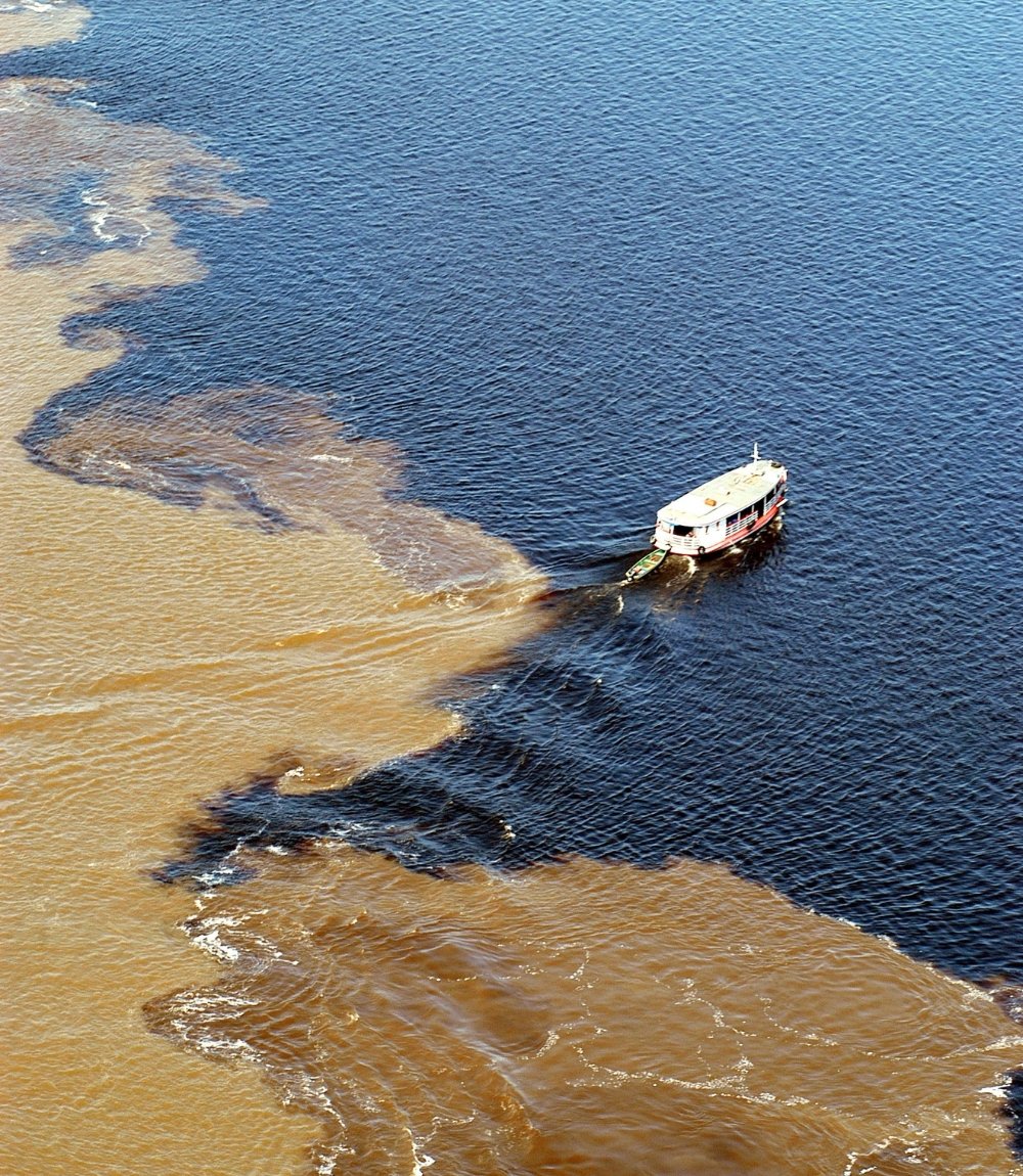 Bateau traversant la ligne entre le rio Negro sombre et le Solimões brun sableux à la Rencontre des eaux