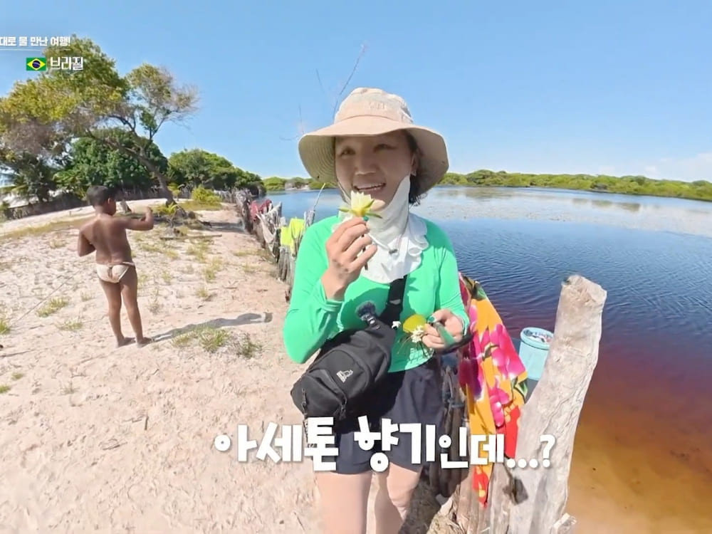 Jihee Yeon holding small yellow flowers by the water, with a local child in the background