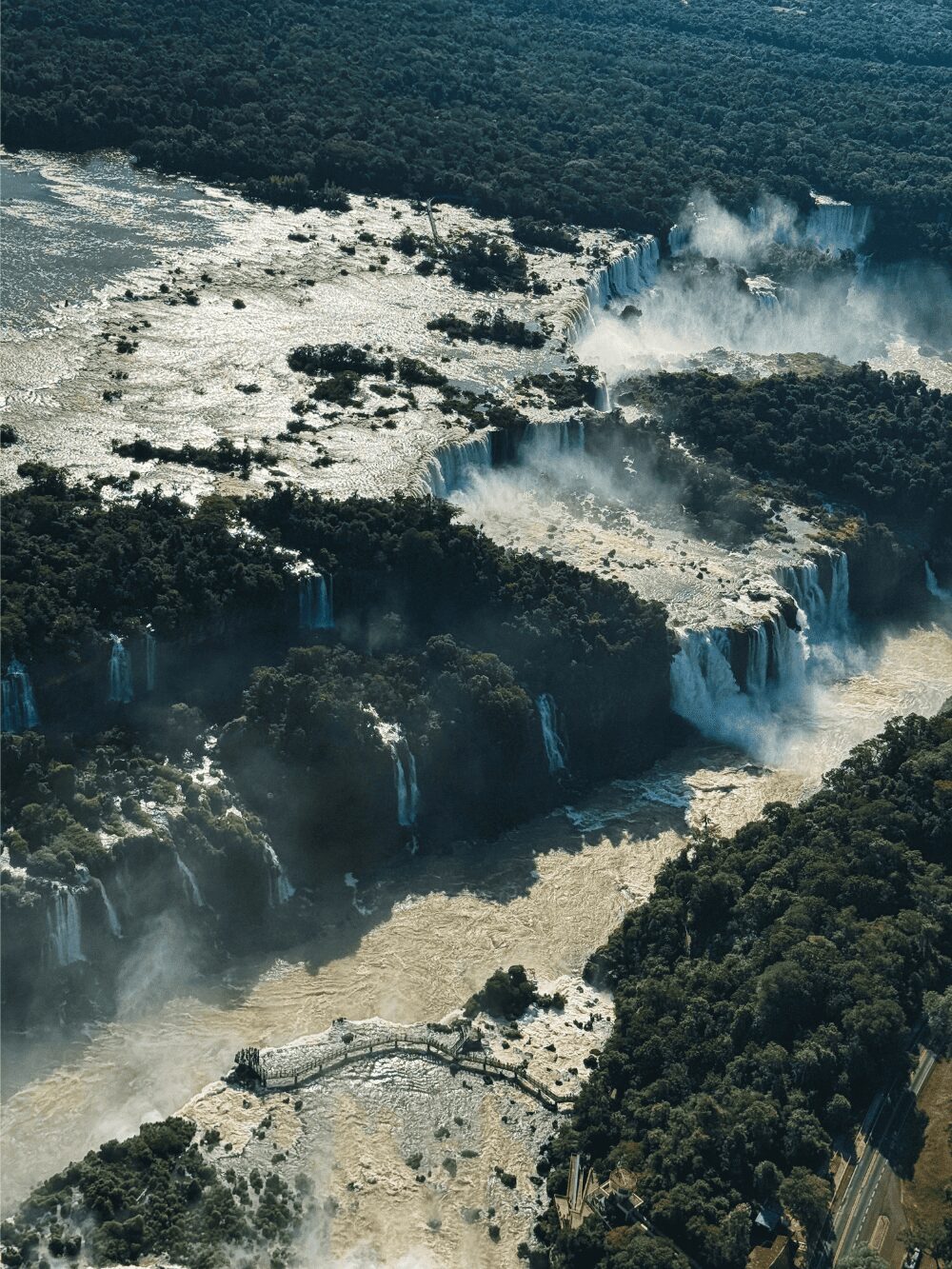 Vue aérienne des chutes d'Iguazu, avec des dizaines de cascades plongeant dans la gorge et une passerelle au-dessus du fleuve