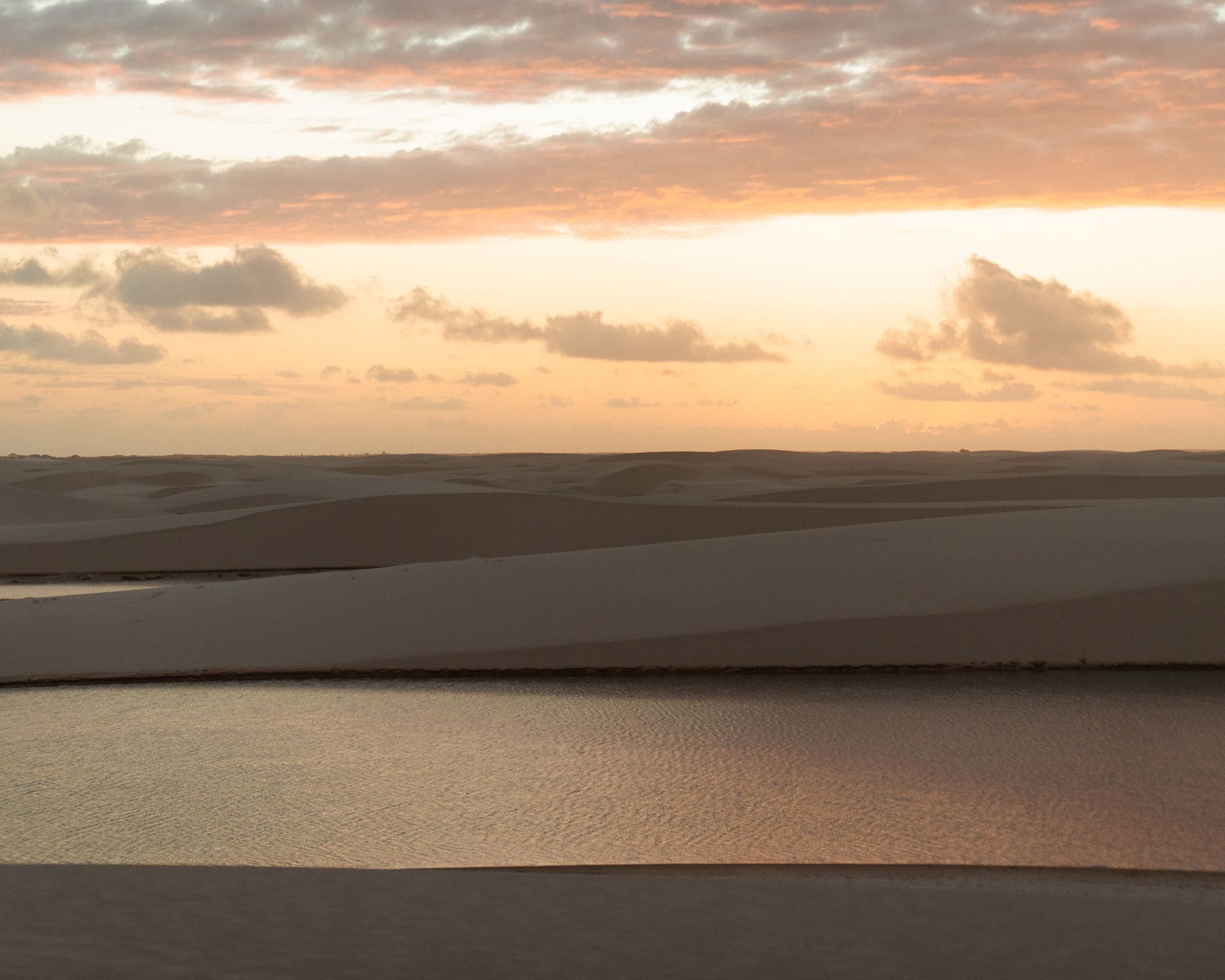 Ciel rose au coucher du soleil sur les dunes de sable blanc et une lagune d’eau de pluie aux Lençóis Maranhenses