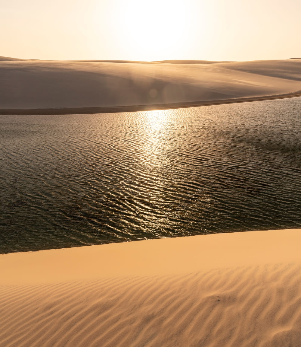 Lumière dorée du soleil reflétée sur une lagune entre des dunes ridées par le vent aux Lençóis Maranhenses