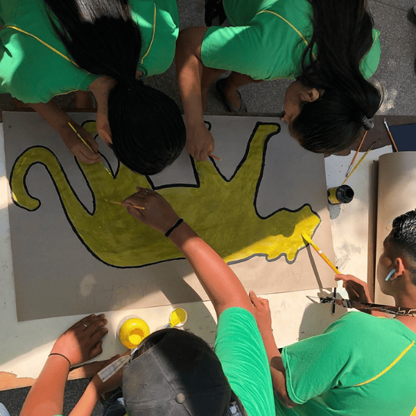 Des élèves en tee-shirt vert peignent un grand jaguar jaune lors d’un atelier d’éducation à l’environnement