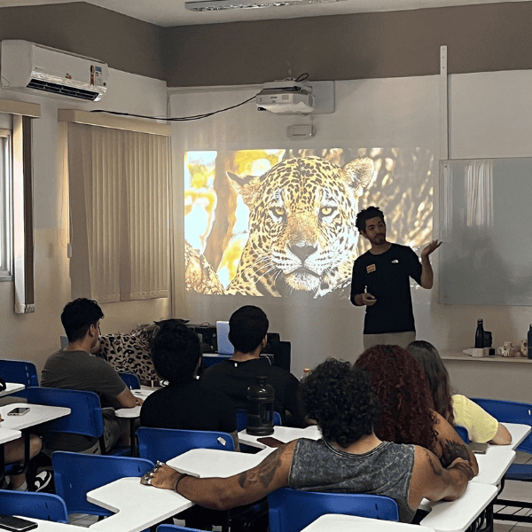 Un membre d’Onçafari anime une intervention devant une salle pleine, une photo de jaguar projetée au mur