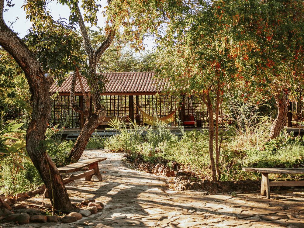 Allée de pierre dans un jardin du Cerrado menant à la véranda avec hamac de la Pousada Trijunção