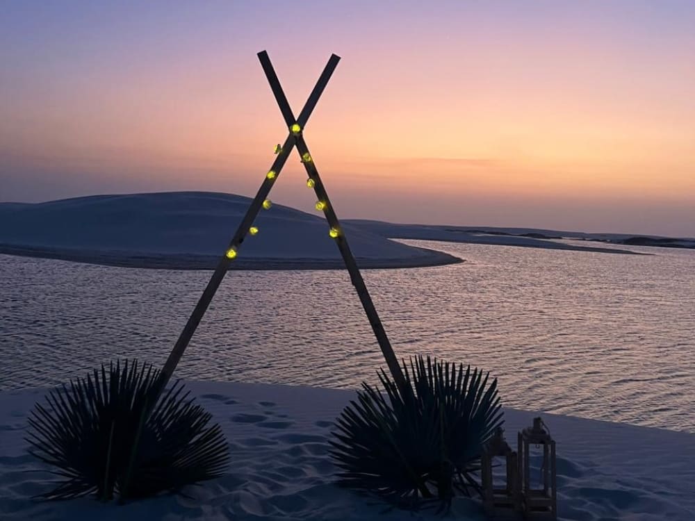 Guirlande lumineuse sur une structure en bois et lanternes au bord d’une lagune au crépuscule aux Lençóis Maranhenses