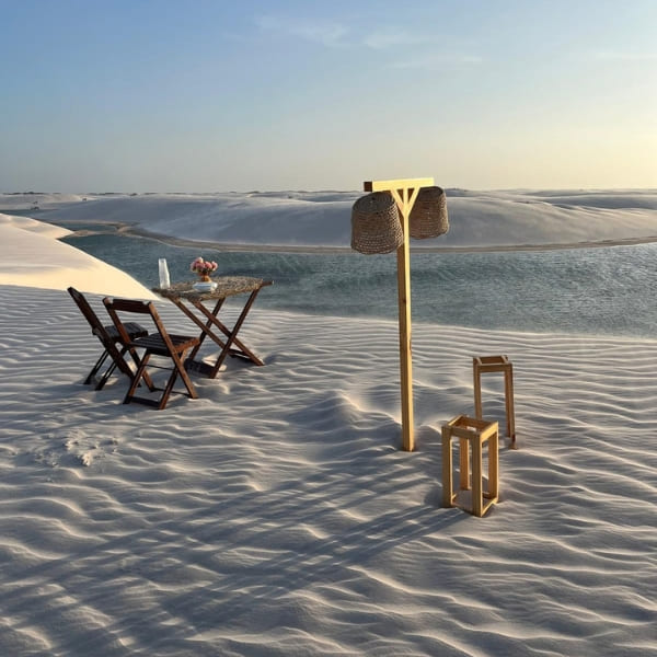 Table pour deux avec fleurs et lanternes installée sur les dunes, au bord d’une lagune des Lençóis Maranhenses
