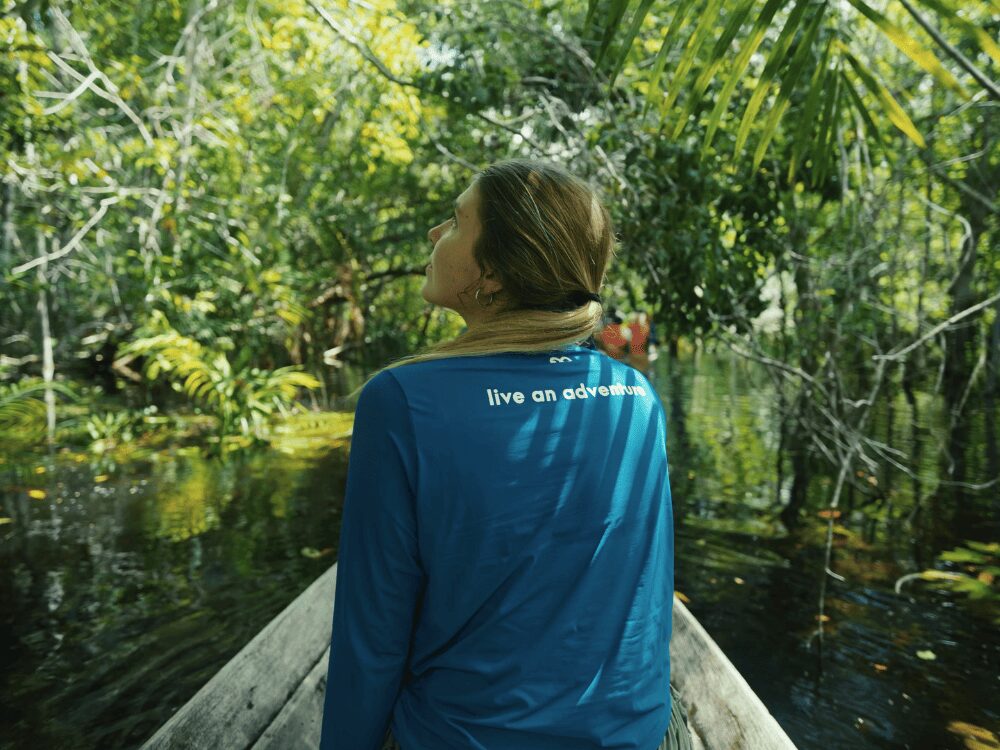 Voyageuse de dos dans une pirogue en bois glissant sur un chenal de forêt inondée lors d’une excursion de plusieurs jours en Amazonie depuis Manaus