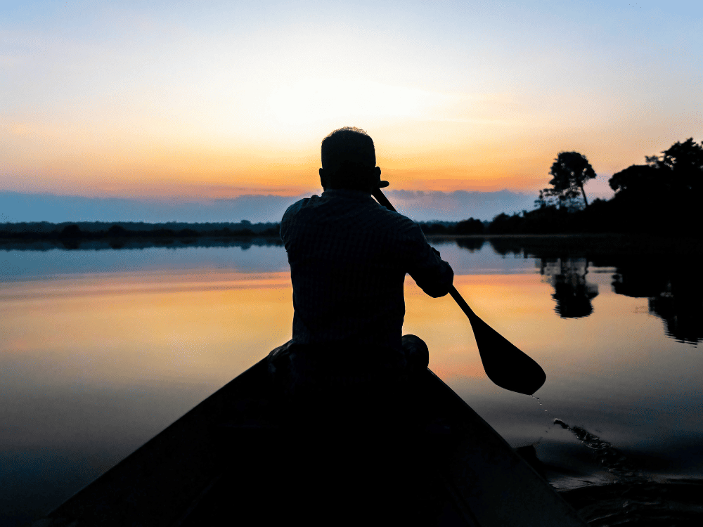 Silhouette d’un homme pagayant en pirogue sur une rivière calme au coucher du soleil, une façon plus lente d’explorer l’Amazonie