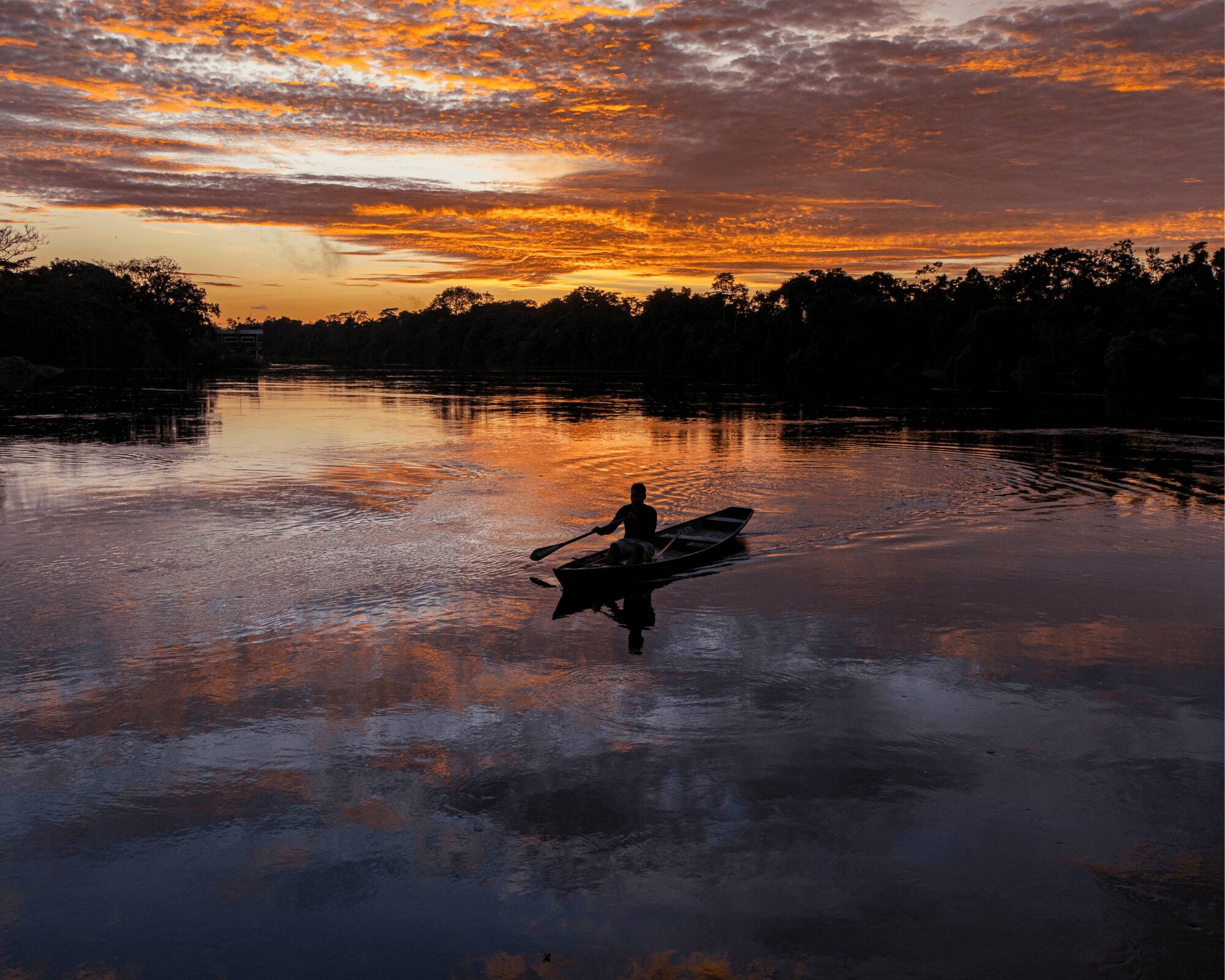 Personne pagayant dans une pirogue en bois sur une rivière calme de la forêt au coucher du soleil, un moment classique d’une excursion en Amazonie depuis Manaus