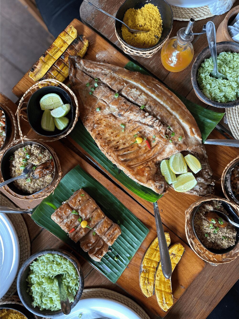 Table de cuisine amazonienne à Manaus : poisson de rivière entier grillé sur feuilles de bananier, banane plantain grillée, farofa, citron vert et riz vert